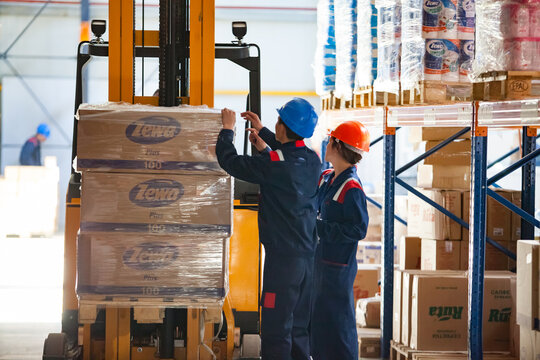 Aktobe, Kazakhstan - May 05, 2012. Two workers hoisting  palette with cardoard boxes pack of toilet paper Zewa. Modern distribution centre and warehouse. 