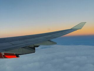 Obraz premium View from the porthole on the wing of an airplane with a red aircraft engine flying above beautiful white clouds.