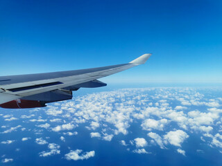 Obraz premium View from the porthole on the wing of an airplane with a red aircraft engine flying over beautiful white clouds and the sea.