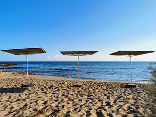 A small sandy beach on the Mediterranean Sea with three square parasols against a blue cloudless sky.