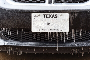 Toned photo frozen Texas license number with icicles. Icy frosty cover Black SUV car bumper and...