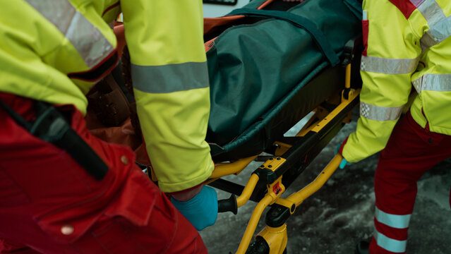 Close Up Shot Of Paramedics Lifting And Pushing A Stretcher Into An Ambulance Car With A Dead Body In The Bag.