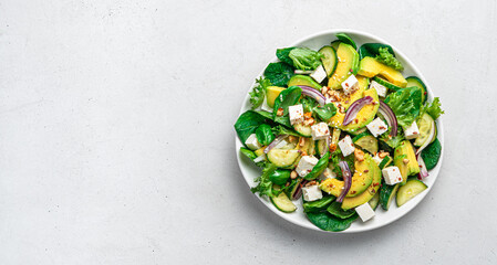 Avocado salad with fresh herbs, feta, cucumber and seeds on a light gray background.
