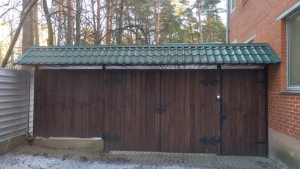 Wooden gates with metal curtains are located between the metal fence and the red brick building and are covered with a metal tile roof