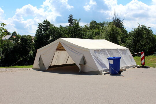 White field hospital tent built by military on paved parking lot and used for COVID-19 coronavirus outdoor testing next to plastic blue garbage container used for medical waste