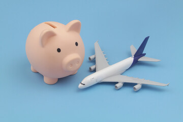 Airplane tickets price and save money concept. Airplane model and piggy bank on blue background.	