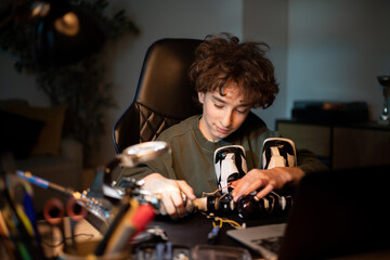 Fototapeta na wymiar Boy works to create remote-controlled robot, uses soldering iron, tools, robotics enthusiast develops skills, learns to tinker