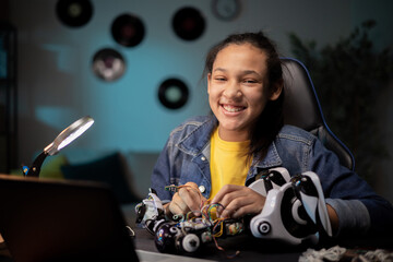 Happy young girl develops robotics skills, fixes electronics that power toy, connects cables,...
