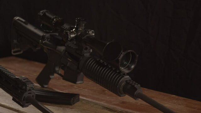 Dolly out of AR 15 rifle with scope, revealing barrel of other rifle on wooden table