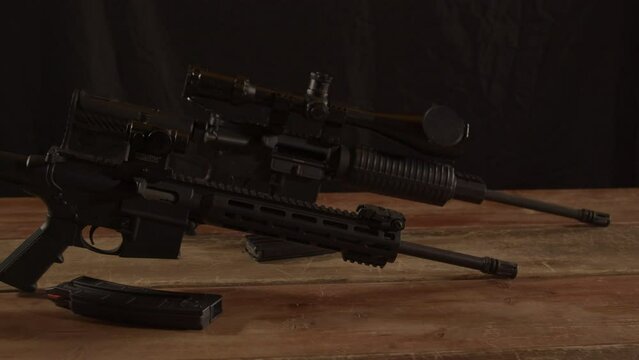 Two types of AR 15 rifles standing on a wooden surface. Slow dolly out