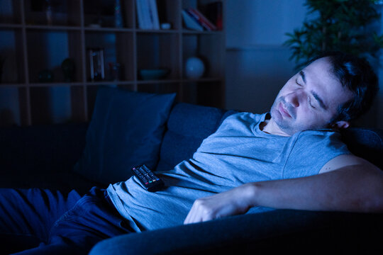 Tired man sleeping at night on the sofa watching tv at home
