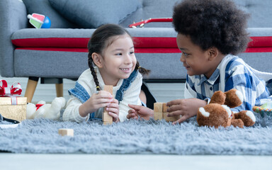 Cute little Caucasian and African kids girl and boy lying on floor smiling and playing toys build...