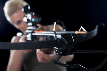 Young woman shooting with crossbow isolated on black background.