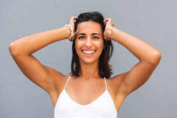 smiling young woman with hands on head by gray wall