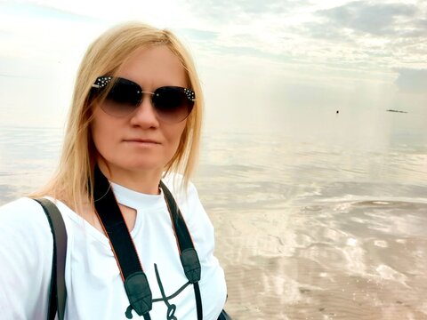 A beautiful adult woman takes pictures of herself, takes selfies. Wearing sunglasses with white hair. The sea is in the background