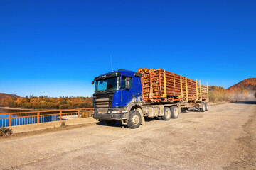 Blue logging truck on forest road in autumn
