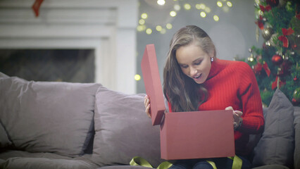 Beautiful woman sitting on couch and opening New Year present box