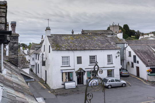 Hawkshead's medieval town square lined by seventeenth century buildings and set below the church of St Michael and All Angels on a cloudy summer's day