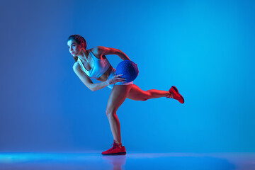 Balance. Young sportive girl training with ball isolated on gradient blue-pink studio background in neon light. Sport, action, fitness, youth concept.