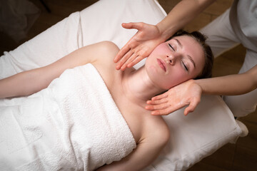 Obraz na płótnie Canvas Woman's face massage in spa salon, top view, massage therapist's hands on girl's face, skin rejuvenation massage, health and youth
