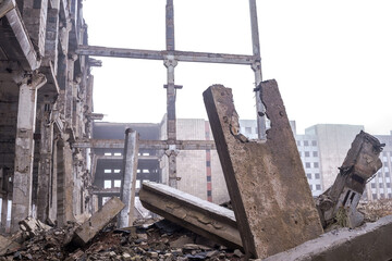 A pile of broken large piles, a broken slab and debris against the background of a destroyed building in the fog. Background