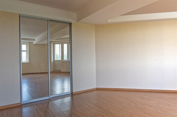 Clean white unfurnished interior with built-in mirror cabinet. Beige wall and brown wood texture floor.