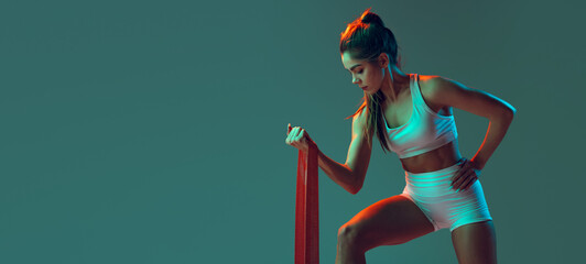 Doing dumb-bell curls. Portrait of sportive woman workout, doing exercises with sports equipment isolated on green studio background in neon light.