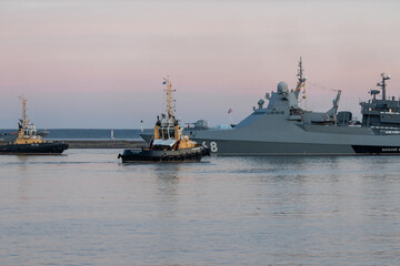 Two naval harbor tugs against the background of warships in the Petrovskaya pier of Kronstadt....