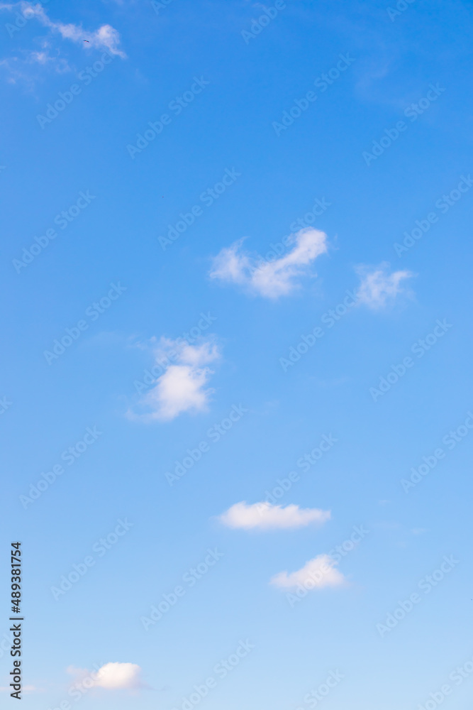 Wall mural blue sky with small white clouds in vertical alignment.