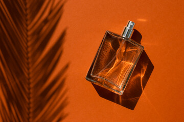 Transparent bottle of perfume on a terracotta color background. Fragrance presentation with...