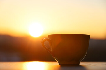 Silhouette of coffee or tea cup on sunrise background. View from the window to morning city