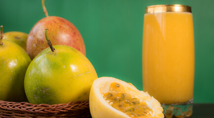 Passion fruit in a basket and its juice on a black wooden table with green background 