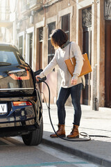 Fototapeta na wymiar Woman stands on the street and plugs a charger to electric car socket.