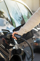 Cropped view woman holding conector plugging in hands to recharge electric car