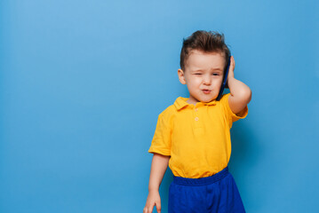 A little boy is talking on a mobile phone. Studio photo on a blue background.