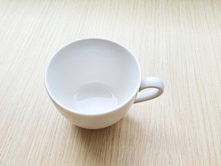Empty white ceramic mug (eardrum) placed on a wooden table. A mug for hot beverages such as coffee, tea, soy milk, chocolate or milk.
