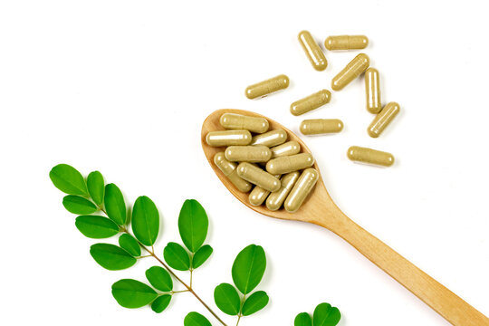 Moringa oleifera capsule on wooden spoon with moringa leaf isolated on white background.