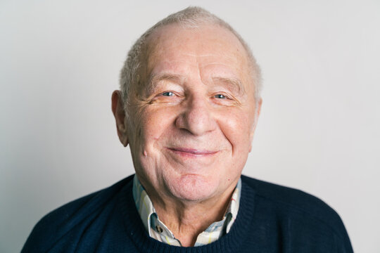 Senior smiling man with gray hair and wrinkles near gray wall