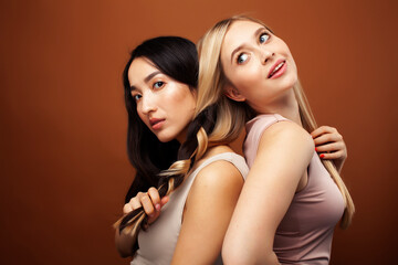 two pretty diverse girls happy posing together: blond and brunette, caucasian and asian on brown...