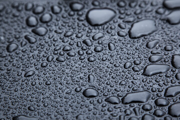 Drops of rain on a black rubber surface close-up.
