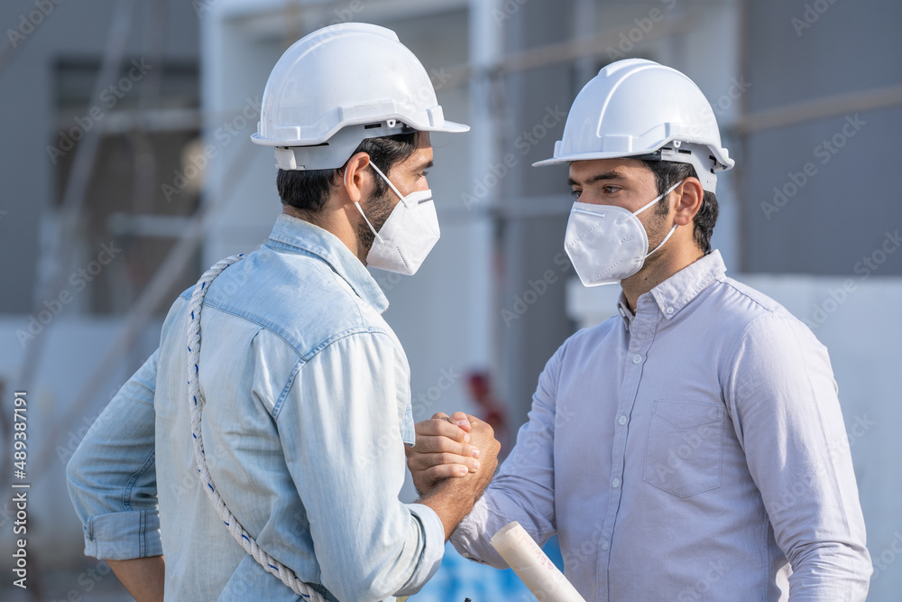 Poster engineer and architect wearing protective mask to protect against covid-19 are shaking hands after f