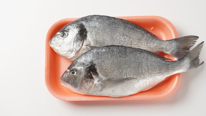 Raw fresh uncooked dorado or sea bream fish with lemon, herbs,  cherry tomatoes and spices on  black background