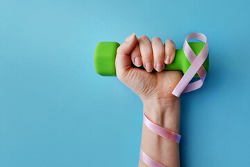 A dumbbell with a pink ribbon in the hands of a woman. A symbol of victory over breast cancer
