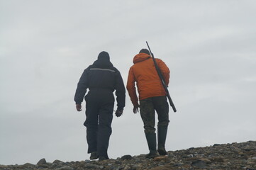 dwaj mężczyźni tyłem idący na polowanie z bronią palną w zimie na grenlandii