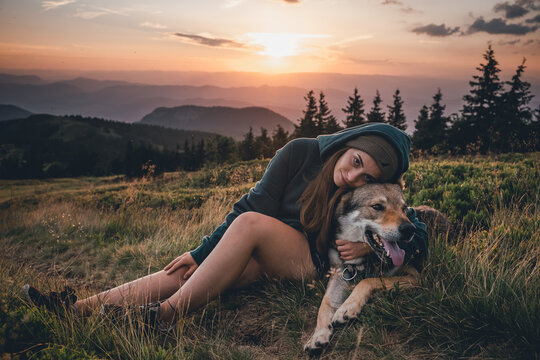 girl with a wolfdog sitting next to each other on a meadow in the mountains at sunset