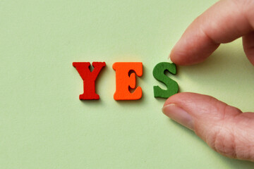 The word yes is made of wooden letters on a light green background