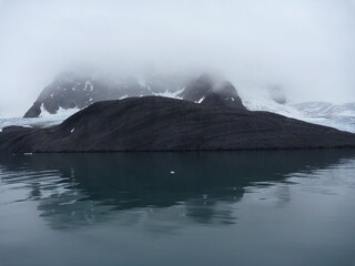 malownicze ośnieżone góry we mgle odbijające się w tafli wody w regionie svalbard na arktyce