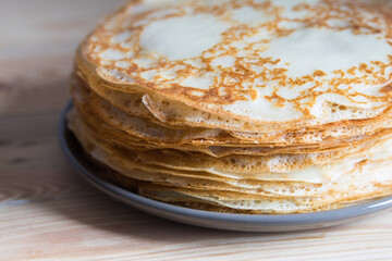 Stack of russian thin pancakes blini on grey plate on wooden background. Close-up, selective focus