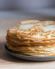Stack of russian thin pancakes blini on grey plate on wooden background. Close-up, selective focus