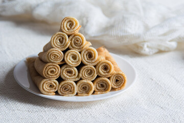 Stack of russian thin rolled pancakes blini on white plate on light rustic background. Close-up,...